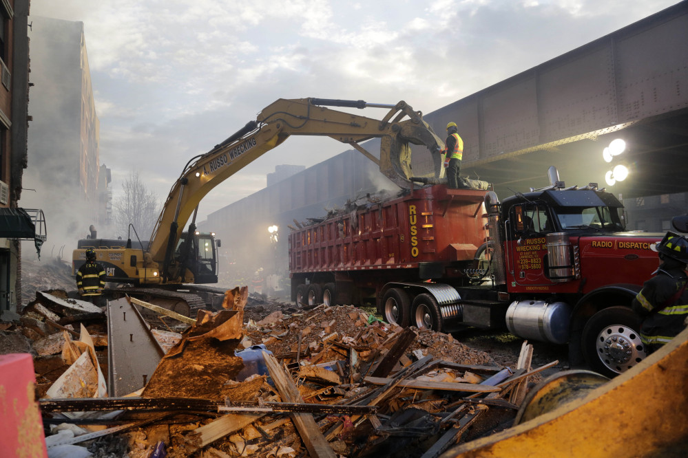 An excavator removes smashed bricks, splinters and mangled metal from the explosion site Thursday.