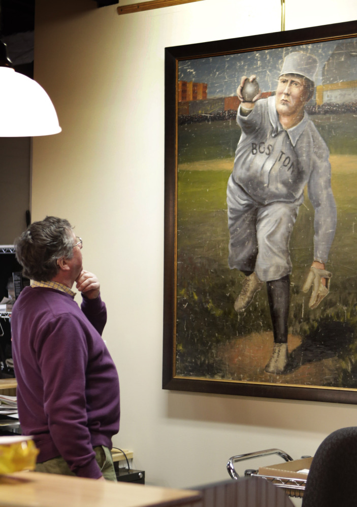 Auctioneer Floyd Hartford examines a 1910 painting of Cy Young in the uniform of the Boston Americans at the Saco River Auction House in Biddeford on Tuesday.