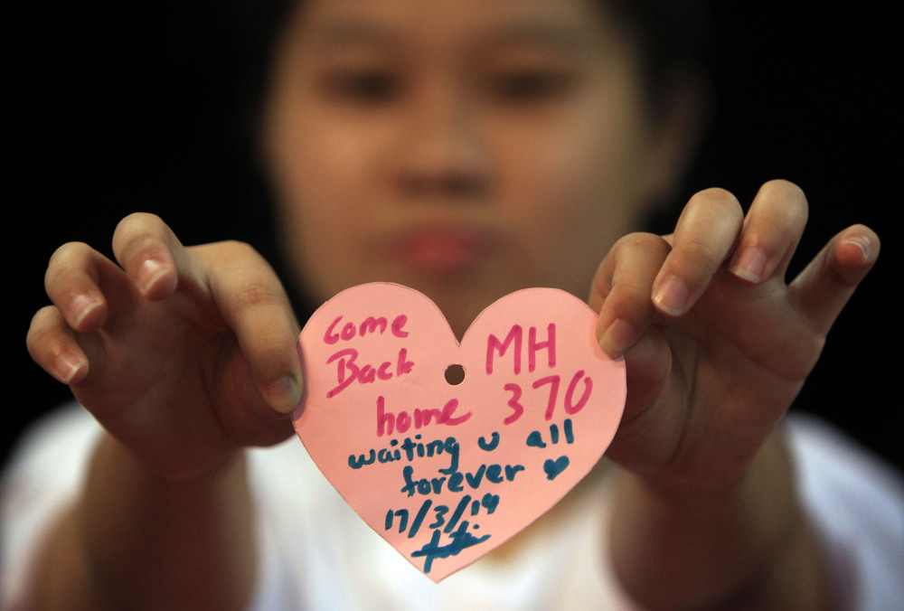 A woman holds a heart-shaped paper with messages for passengers aboard a missing Malaysia Airlines plane, as she poses for a photo during an event in Kuala Lumpur, Malaysia, on Monday.