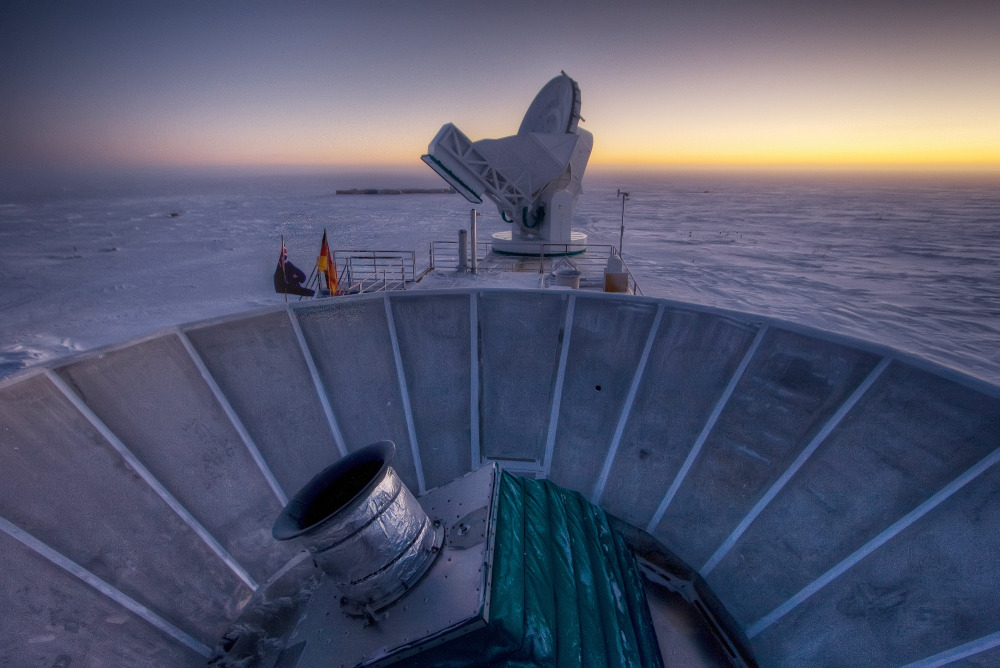 The sun sets behind the BICEP2 telescope, foreground, and the South Pole Telescope in Antarctica. In the faint glowing remains of the Big Bang, scientists found “smoking gun” evidence that the universe began with a split-second of astonishingly rapid growth from a seed far smaller than an atom.