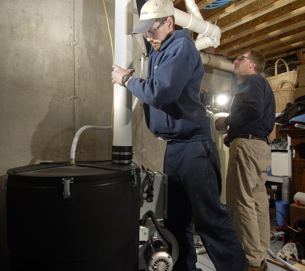 RADON TEST: Shawn Garrity, left, and Scott King of Air & Water Quality Inc., of Freeport, install a radon gas treatment unit in a Maine home in a 2007 file photo. Maine law requires landlords to test for radon in all buildings with rental units, but it’s still unclear what agencies will enforce the penalties if they don’t.