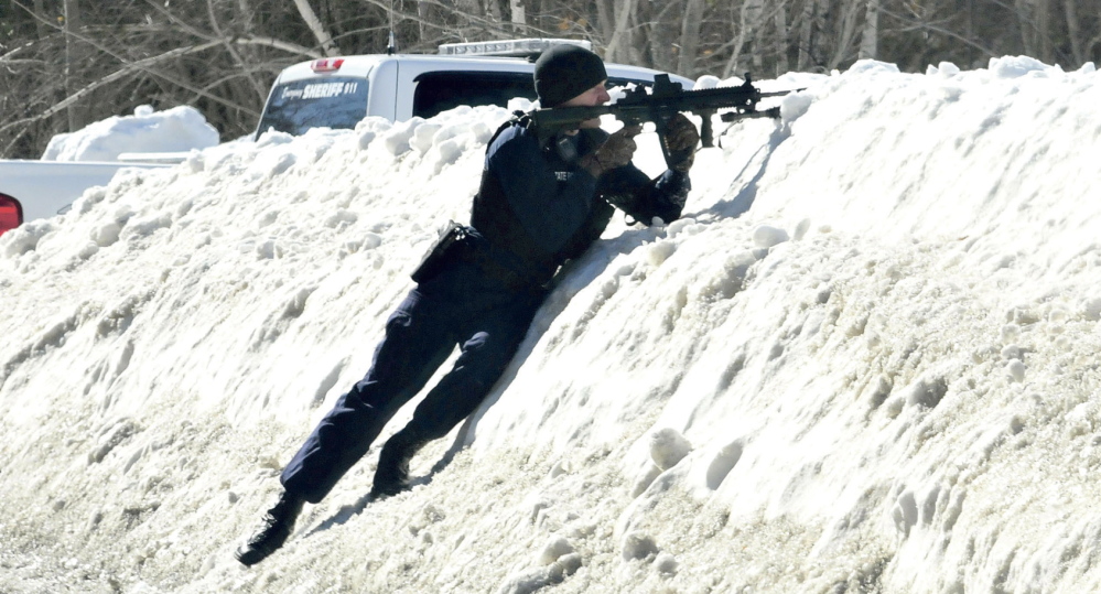 ARMED: Trooper Scott Duff trains his rifle toward the home of Michael Smith as other police called for him to come out of the home in Norridgewock on Tuesday. Tree workers called police earlier after they encountered Smith regarding cutting wood under power lines and mistook a pistol tattoo as a real firearm.