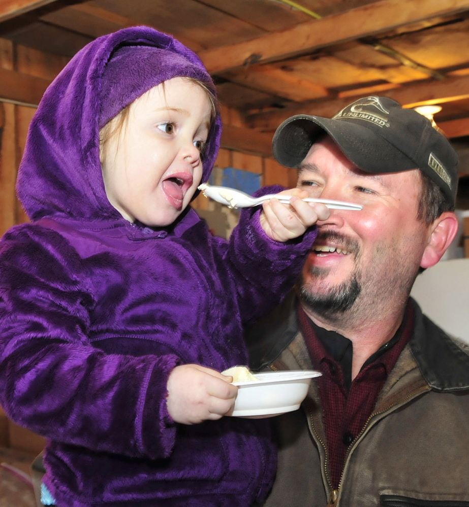 YUMMY: Wayne Smith holds his granddaughter Haleigh Hutchins as she enjoys some ice cream topped with maple syrup during a Maine Maple Sunday event at the Rodney Hall farm in East Dixfield on Sunday.