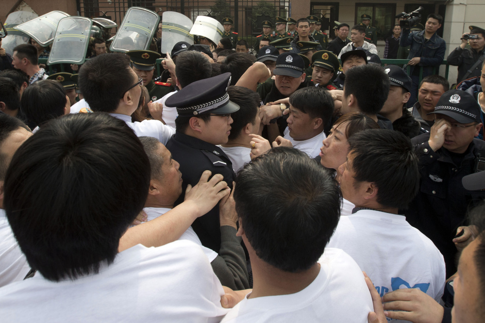 Relatives of Chinese passengers onboard the Malaysia Airlines plane MH370 scuffle with Chinese police officers outside the Malaysian embassy in Beijing, China, Tuesday, March 25, 2014. Furious that Malaysia has declared their loved ones lost in a plane crash without physical evidence, Chinese relatives of the missing marched Tuesday to the Malaysia Embassy, where they threw plastic water bottles, tried to rush the gate and chanted, “Liars!”