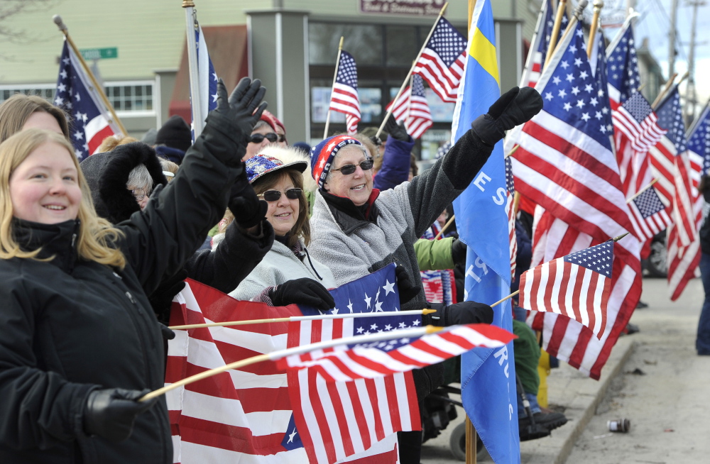 Cathy Cunningham, in the center of the photo, raises a mitten-covered hand in salute as she and dozens of other supporters wave at passing vehicles in support of the Freeport Flag Ladies, including Carmen Footer, who is recovering from heart surgery and missed the weekly ritual.