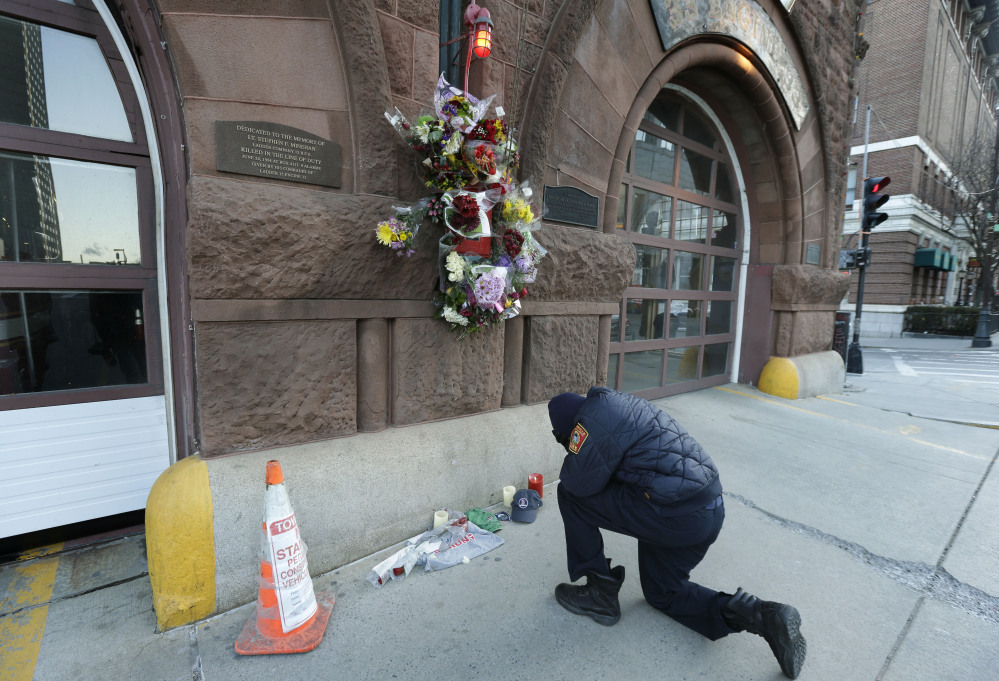 Somerville, Mass., firefighter Earl Johnson kneels to pray in front of a makeshift memorial on the front of fire station Engine 33 on Thursday in Boston. Fire station Engine 33 was the station of fallen firefighters Lt. Edward J. Walsh and Michael R. Kennedy.