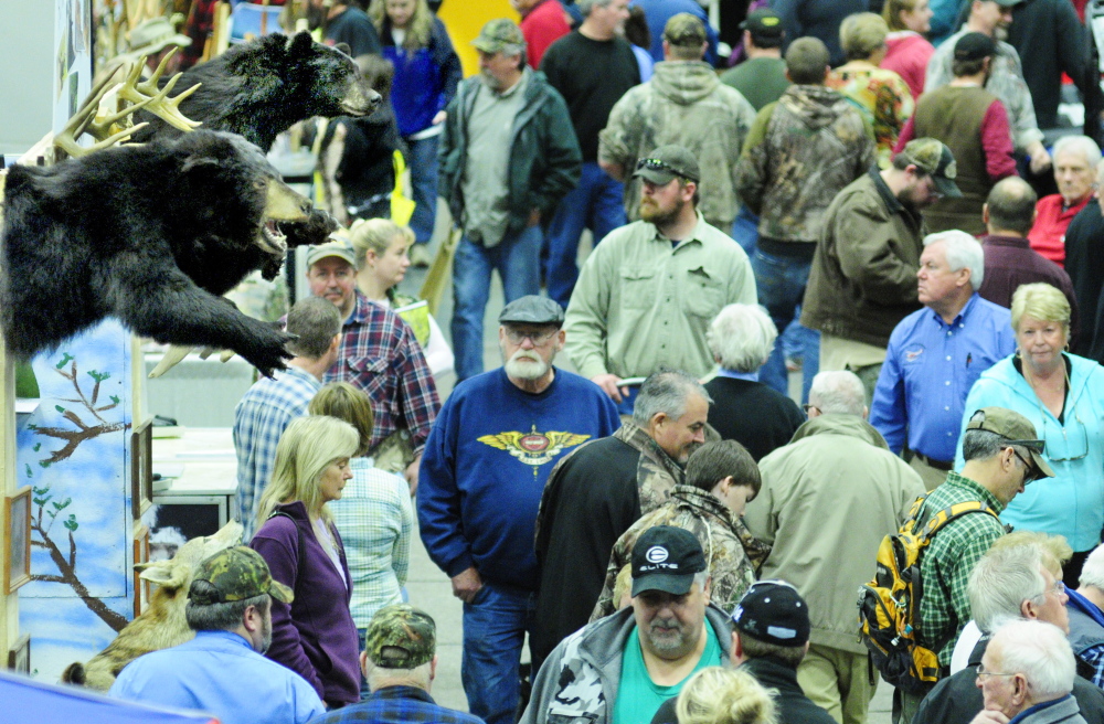 A symbolic presence: Showgoers walk past a booth with stuffed bears on display Saturday during the Maine Sportsman’s Show in the Augusta Civic Center.