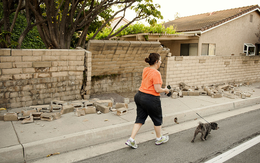 A woman walks her dog past a broken block wall in Fullerton, Calif., on Saturday.