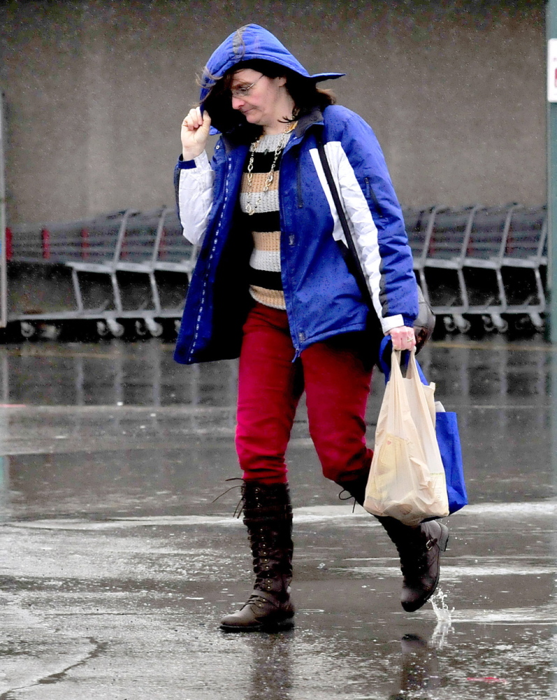 Staff photo by David Leaming LIQUID SNOW: Sarah Wright leans into the blowing rain and shields her face with a hood at Elm Plaza inWaterville on a wet Sunday, March 30, 2014. "This rain is better than snow," wright said.