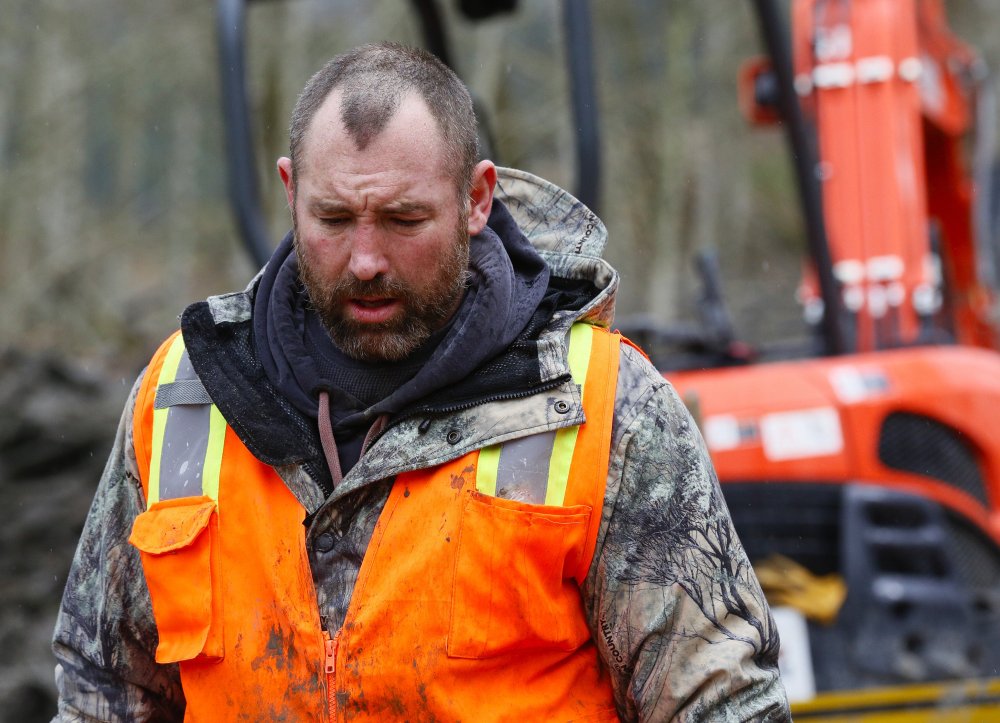 A weary searcher bows his head as he walks out of the west side of the mudslide site with a small saw on Highway 530 near mile marker 37 in Arlington, Wash., on Sunday. Periods of rain and wind hampered efforts for two days.