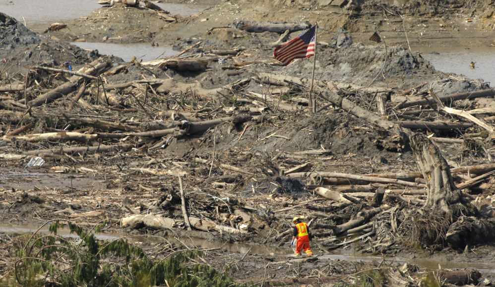 A searcher walks through a channel of water as a flag flies in the debris field Monday near Darrington, Wash., at the site of the massive mudslide that hit the nearby community of Oso,Wash., on March 22.