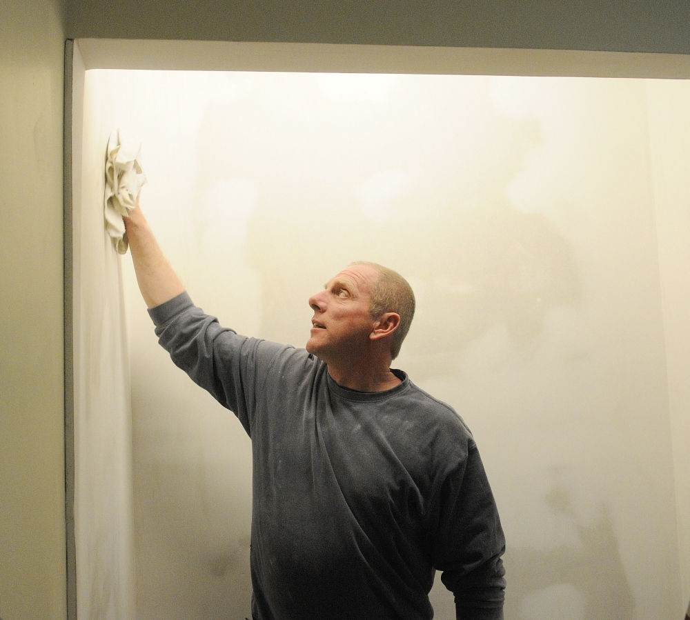 FOR PETS AND AMY: After sanding the wall, Steve Gayne, owner of S n S Multitasking, wipes off dust before painting a wall in the room he is renovating for the Amy Buxton Pet Pantry at South Parish Congregational Church in Augusta.