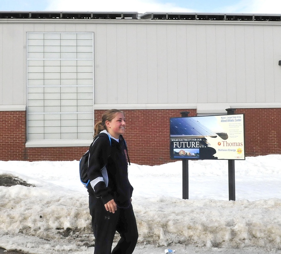 Thomas College student Scarlett Stevens walks past a sign about the solar energy that comes from the panels covering the Alfond Athletic Center at the Waterville campus March 10. Central Maine Power has informed customers that produce their own energy that rates will increase on power supplied by the electricity company.