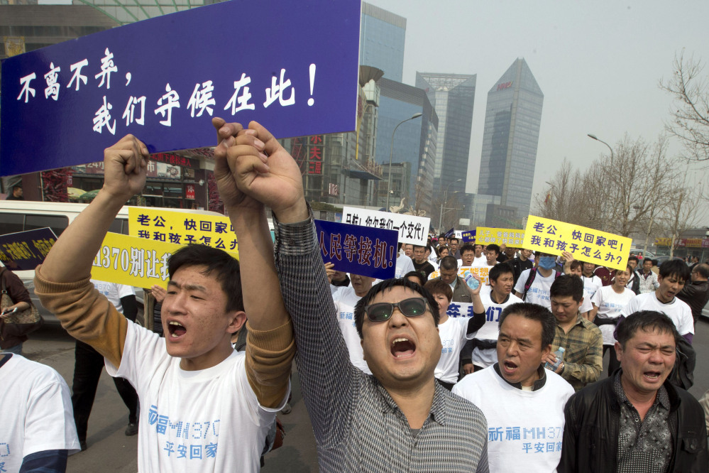 In this Tuesday, March 25 file photo, Chinese relatives of passengers onboard the missing Malaysia Airlines plane, flight MH370, shout in protest as they march towards the Malaysia embassy in Beijing, China. Authorities have been forced on the defensive by the criticism, the most forceful of which has come from a group of Chinese relatives who accuse them of lying about - or even involvement in - the disappearance of Flight 370. The blue placard reads: “We won’t leave or ditch you, we will wait right here.”