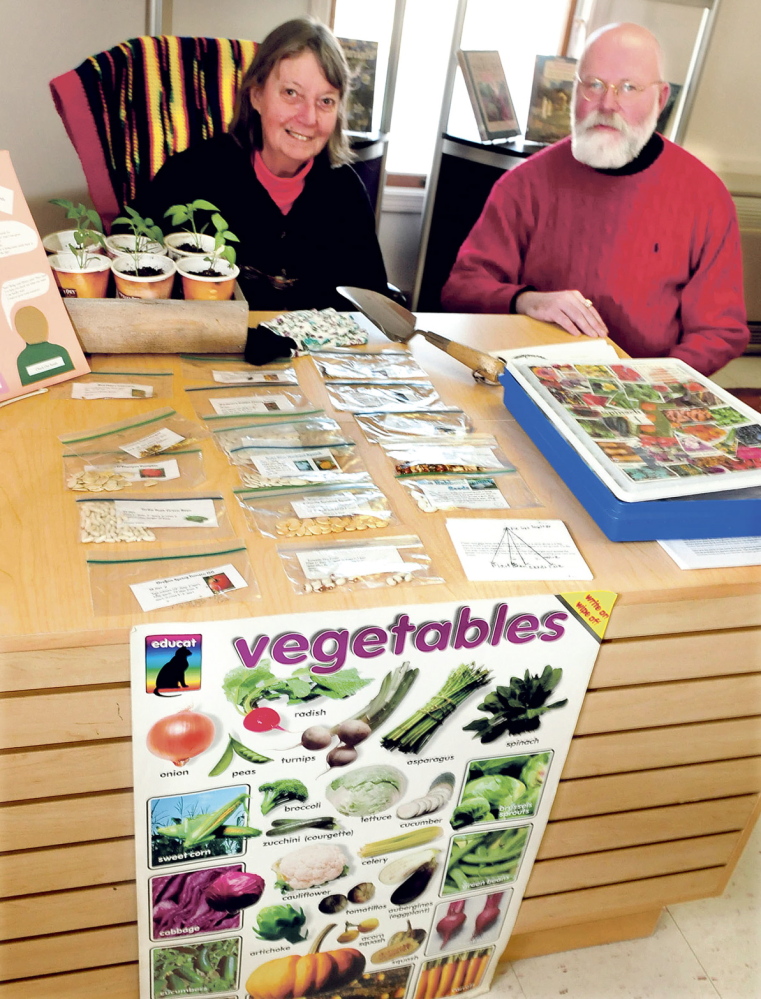 RETURN POLICY: Norridgewock Library Chairman of the Board Sallie Wilder and Librarian Kent Sinclair sit behind a display of seeds, information and gardening books last week. This is the second year of the seed program, where patrons with library cards can select packets of seeds and raise vegetable gardens at their homes.
