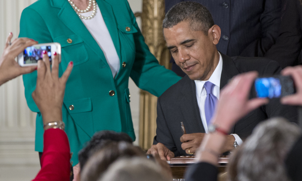 As members of the audience take photos, President Barack Obama signs new executive actions to strengthen enforcement of equal pay laws for women on Tuesday in the East Room of the White House during an event marking Equal Pay Day.