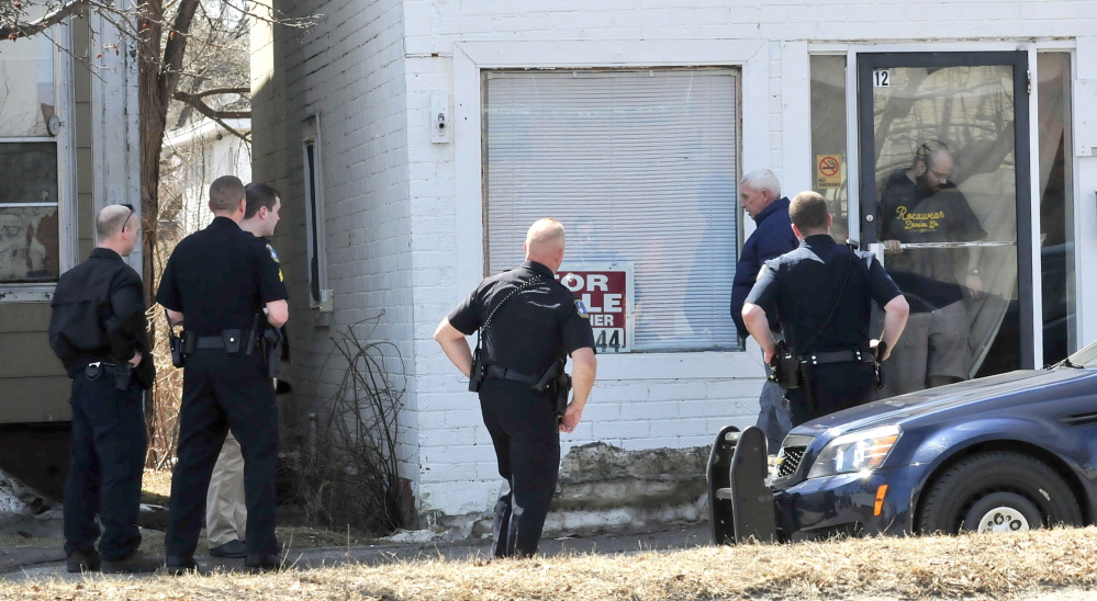 QUESTIONS: Waterville Detective Alan Perkins walks away after speaking with an occupant, in doorway, at 12 Spring St. on Thursday. Several officers and detectives surrounded the building and later arrested Peter Corson after he came out.