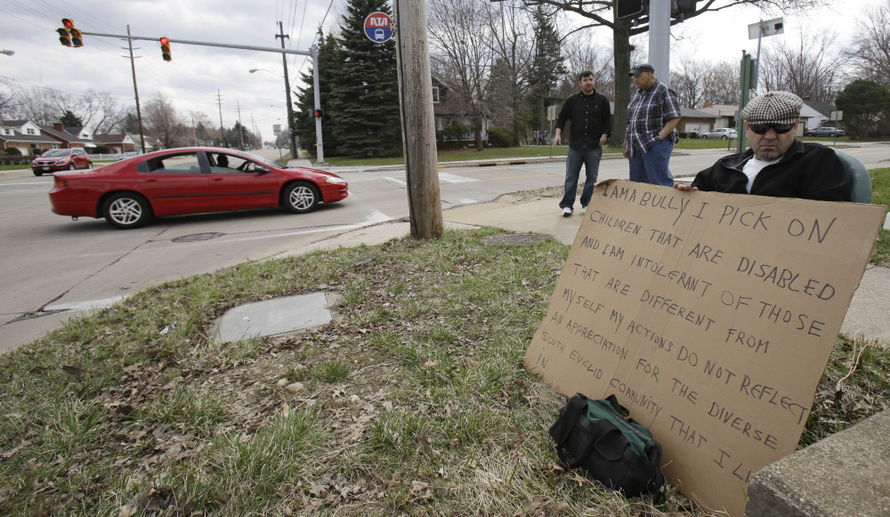 Edmond Aviv sits on a street corner holding a sign Sunday in South Euclid, Ohio, declaring he’s a bully, a requirement of his sentence because he was accused of harassing a neighbor and her disabled children for the past 15 years.