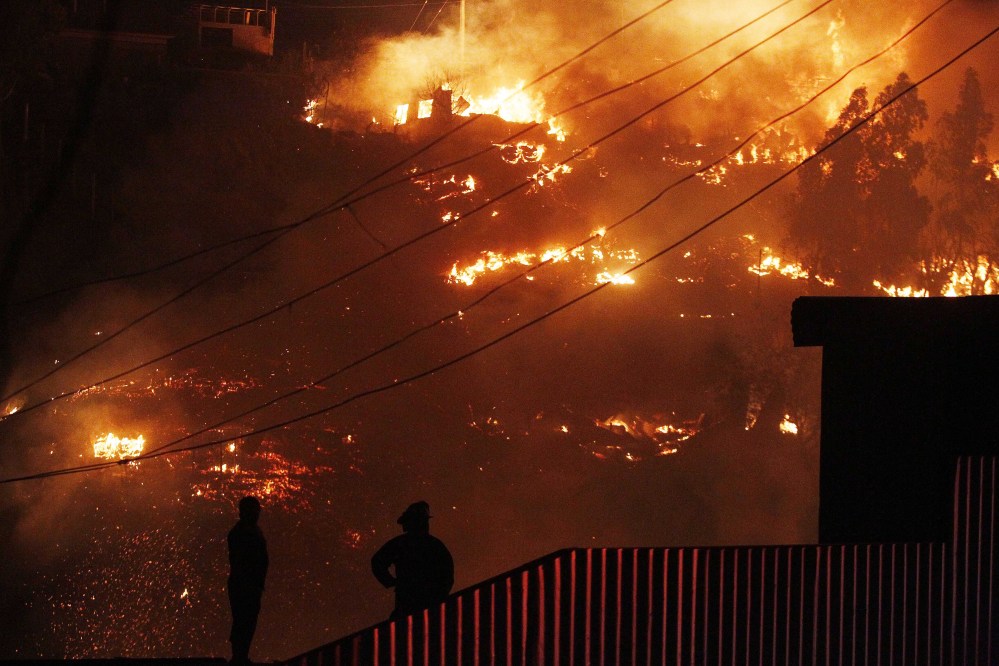 Emergency responders watch as an out-of-control fire destroys homes in the city of Valparaiso, Chile, Sunday. Firefighters struggled for a second night to contain blazes that reached this port city, killing at least a dozen people, destroyed hundreds homes and has forced the evacuation of thousands.