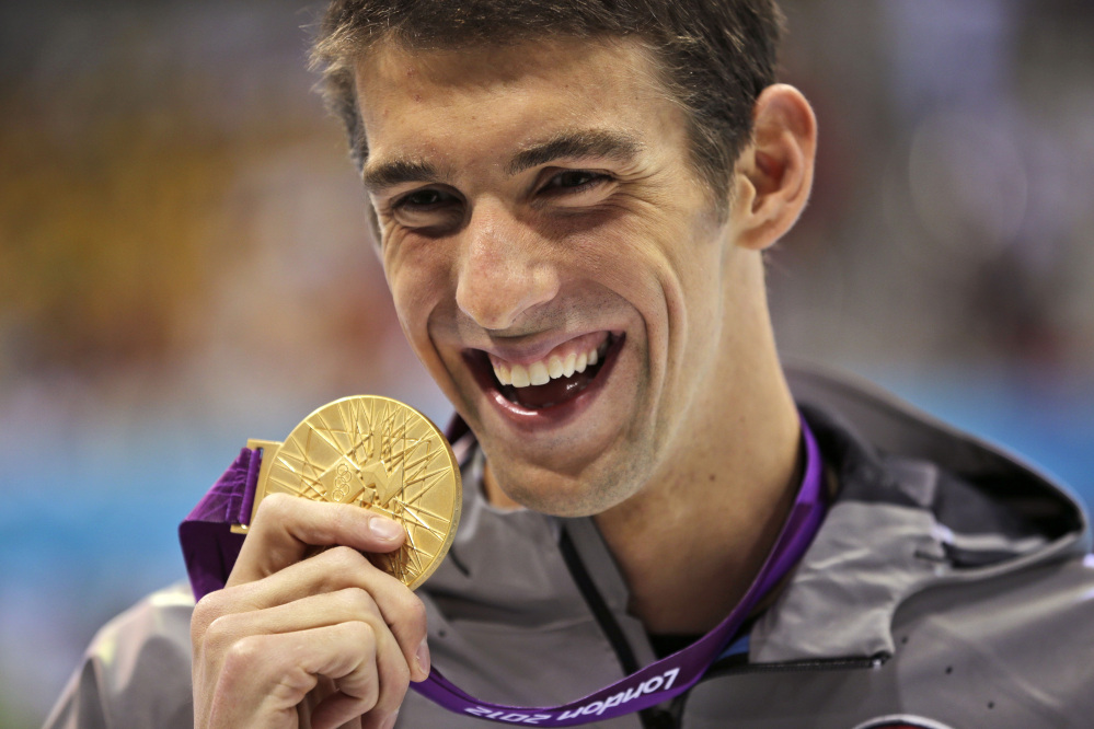 Michael Phelps displays his gold medal for the men’s 100-meter butterfly swimming final at the 2012 Summer Olympics in London, in this Aug. 3, 2012, photo.