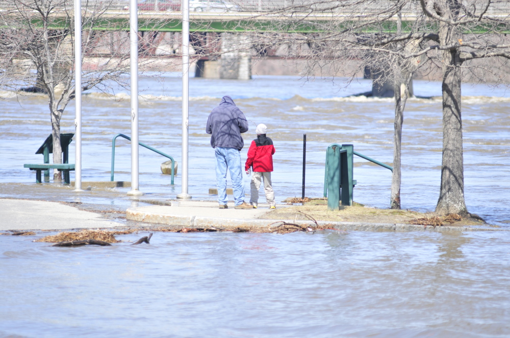 THIS PARK COULD HOLD AN ARK: People look at the rising Kennebec River beside the Augusta Waterfront Park sign on Wednesday in downtown Augusta. The river was at 16 feet around 2 p.m. and predicted to rise another few feet later in the evening.