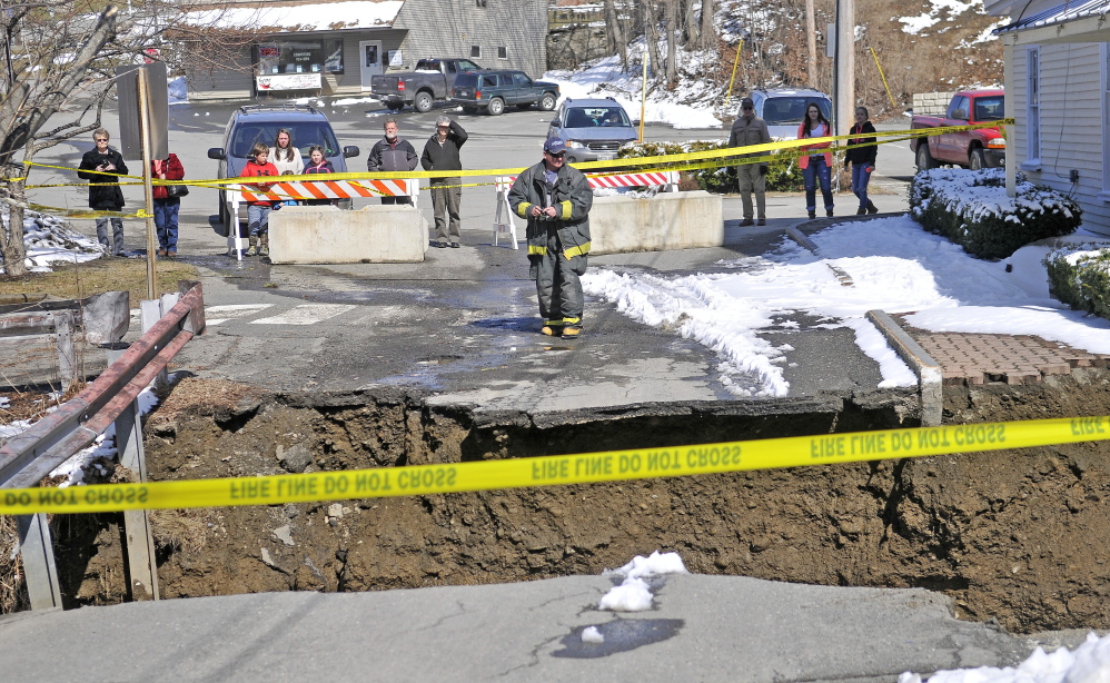 WASHED OUT: A firefighter stands at the edge of the washed-out connector street between Main and Water streets Wednesday in downtown Dexter.