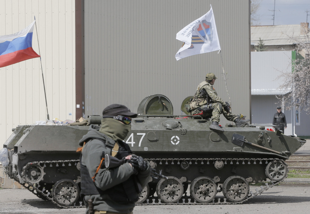 A masked gunman guards combat vehicles with Russian and Donetsk insurgency army flags and gunmen on top, parked in downtown of Slovyansk on Wednesday. One of the on those vehicles wore a St. George ribbon attached to his uniform, which has become a symbol of the pro-Russian insurgency in eastern Ukraine.