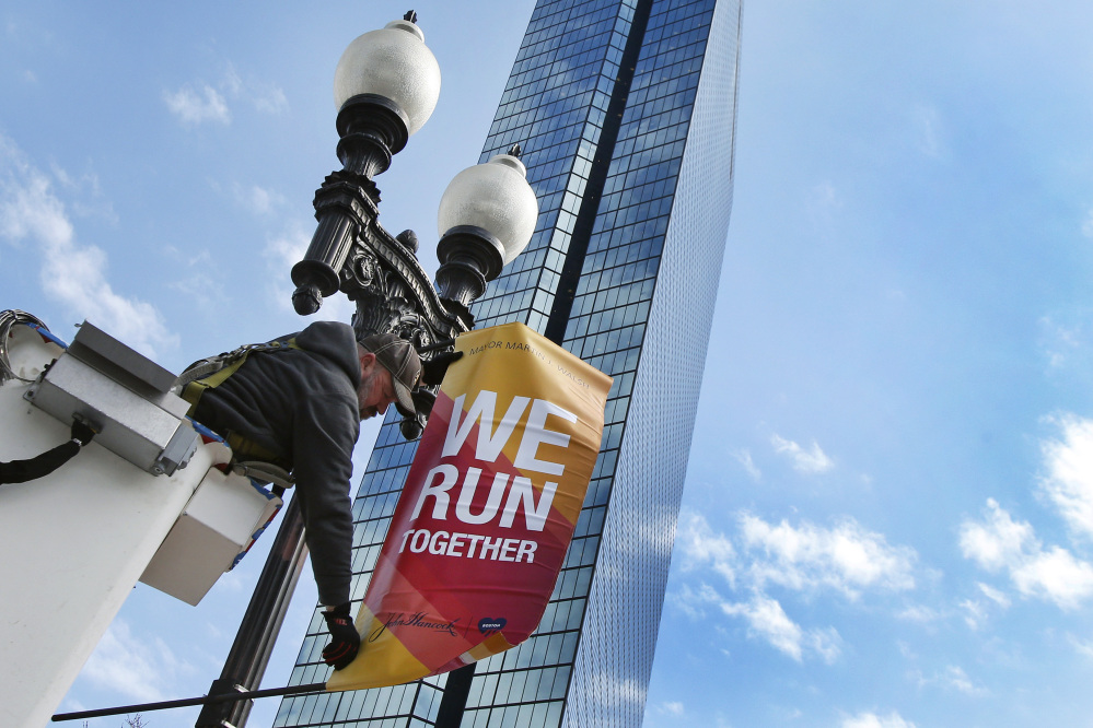 Charlie McCarthy hangs a banner in March announcing the Boston Marathon on a lamppost along Boylston Street in Boston. More runners and more visitors than ever are expected in Boston for the marathon.