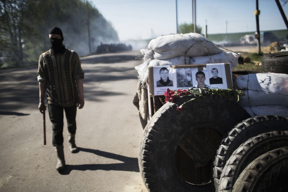 A masked pro-Russia man walks next to a barricade with pictures of three pro-Russia militiamen killed days ago at a checkpoint by Ukrainian forces near Slovyansk, Ukraine, on Thursday.