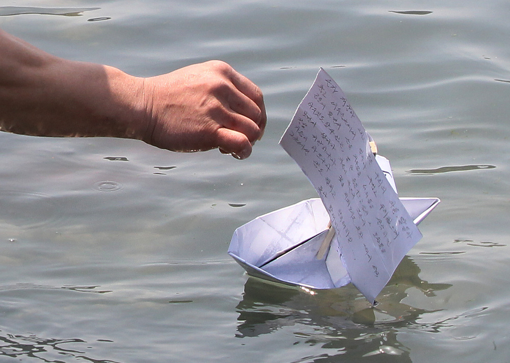 A relative of a ferry passenger releases a paper boat with a message wishing for the safe return of his missing loved one in Jindo, South Korea, Friday