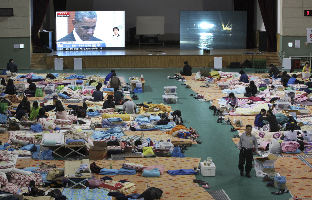 A TV screen shows President Barack Obama paying a silent tribute for the victims of South Korea’s sunken ferry Sewol during a summit meeting with South Korean President Park Geun-hye as relatives of victims looks on at a gymnasium in Jindo Friday.