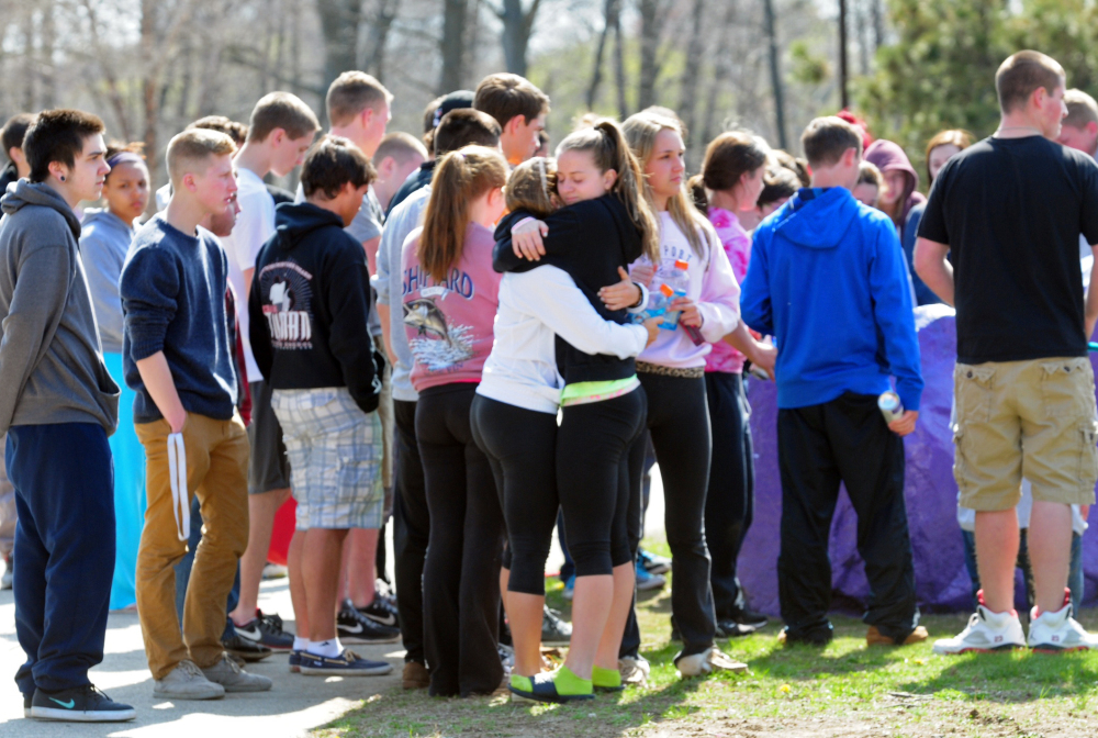 Students hug and spray paint a rock purple outside Jonathan Law High School in Milford, Conn., Friday.