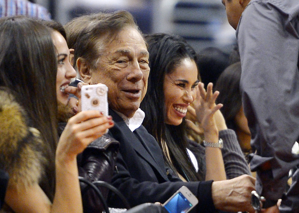 In this Oct. 25, 2013, photo Los Angeles Clippers owner Donald Sterling, center, and V. Stiviano, right, watch the Clippers play the Sacramento Kings in Los Angeles.
