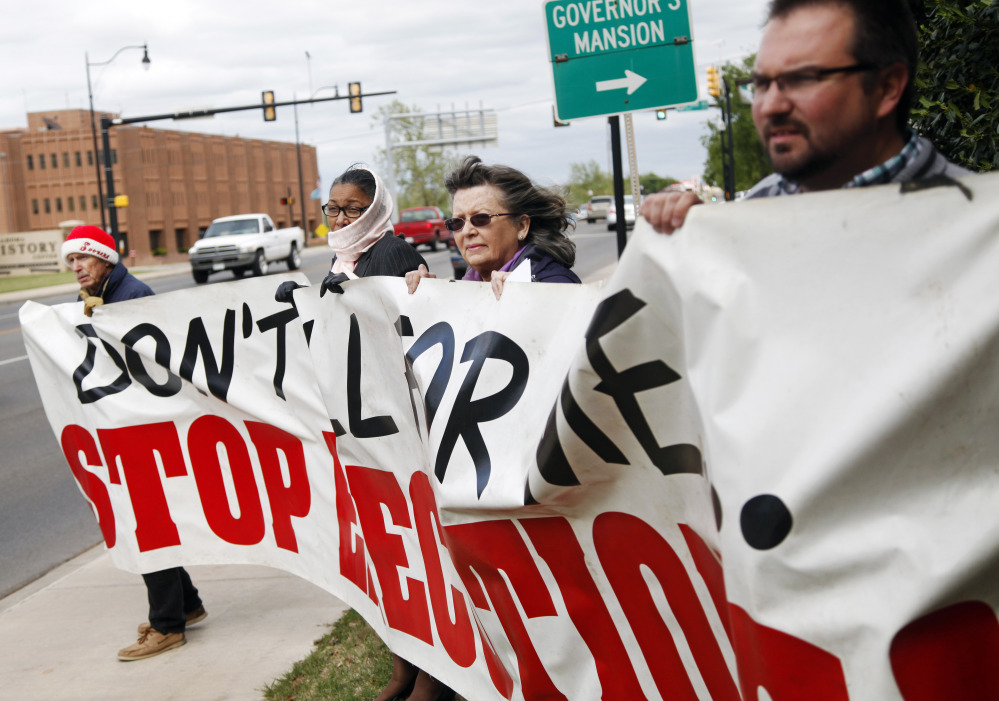John Walters, Jana Lewis-Harkins, Fannie Bates and Aaron Baker, from left, hold a banner during a protest at the Governor’s Mansion in Oklahoma City on Tuesday.