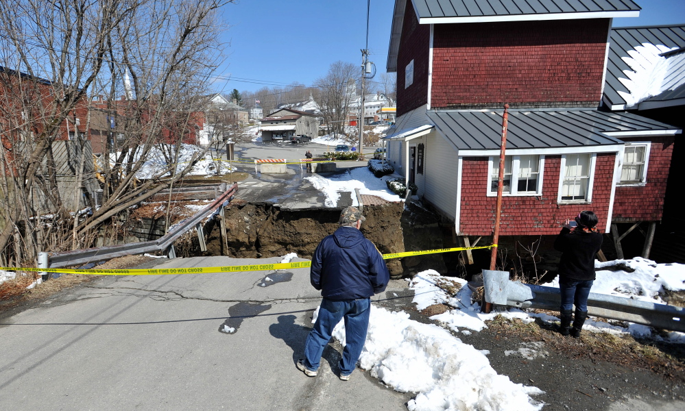 TEETERING: People stand on April 16 by the edge of the washed-out connector street between Main Street and Water Street in downtown Dexter, across the chasm from the Dexter Historical Society Grist Mill Museum, which teetered on the edge of the washout.