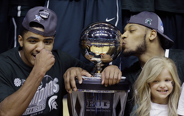 Lacey Holsworth, at right, stands with Michigan State's Gary Harris, left, and Adreian Payne as they pose with a championship trophy in March. Lacey and Payne became friends when he met her in a hospital, and she became an inspiration for the Spartans. Lacey, who was battling cancer, died Tuesday.