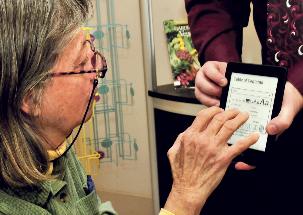 PAGE TURNER: Sallie Wilder takes a swipe at turning pages on a mobile device held by Jared Leadbetter of the Maine State Library during a presentation on using the devices to access e-books at the Norridgewock Public Library on Tuesday.