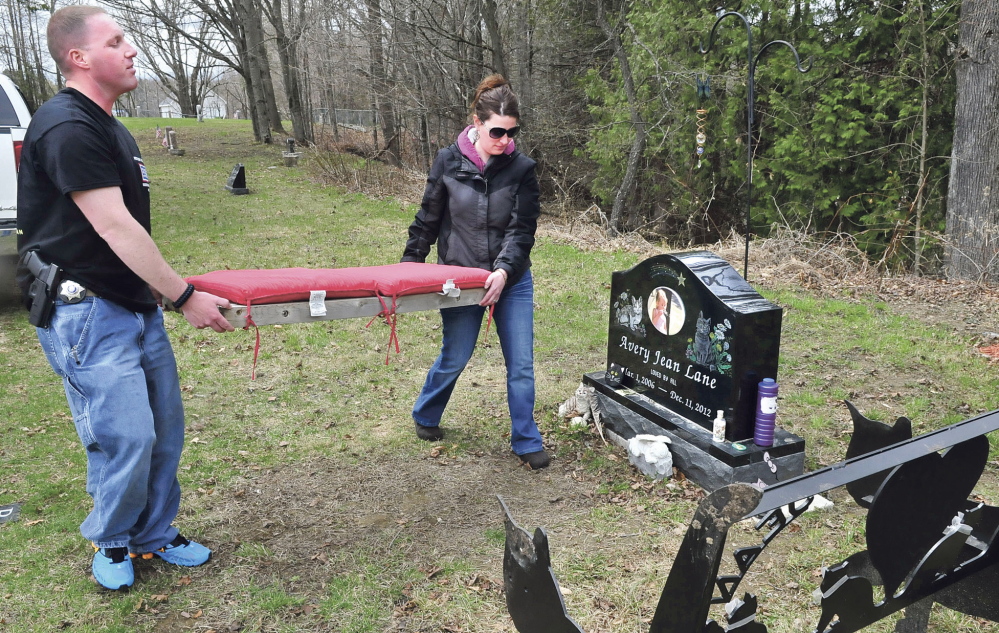 TIDYING UP: Kennebec County sheriff’s Deputy Jacob Pierce and Tabitha Souzer on Tuesday return a cushion to the bench that was thrown down an embankment near the grave site of Souzer’s daughter, Avery Lane, in the Friends Cemetery in Fairfield.
