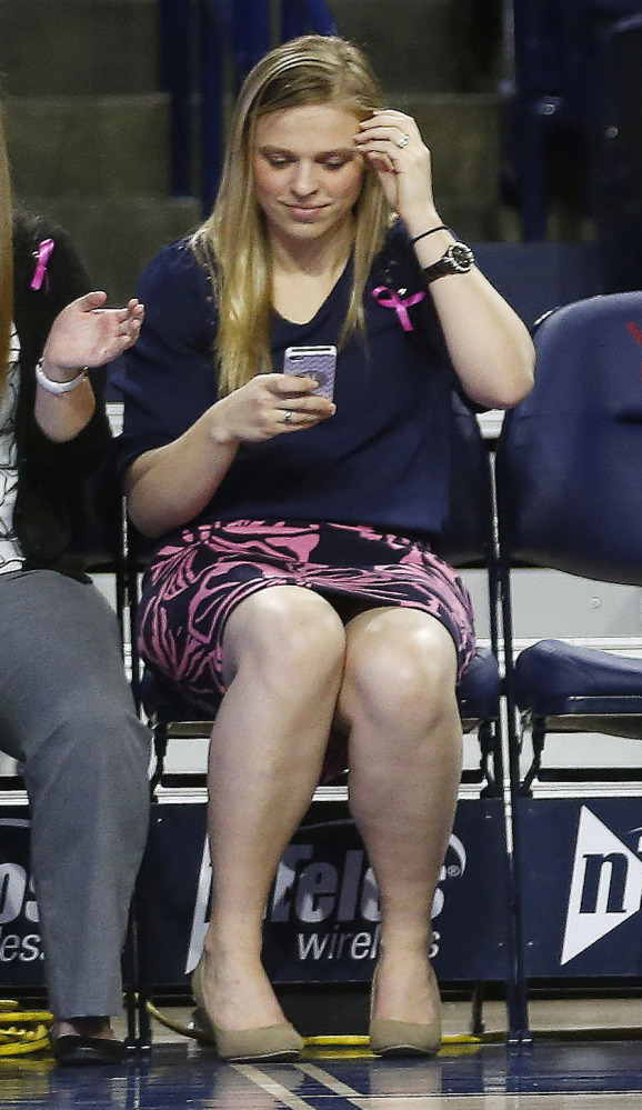 In this Wednesday, Feb. 26, 2014 photo, Natalie Lewis, right, University of Richmond director of basketball operations, looks at her phone as she sits on the bench during a game against Virginia Commonwealth University in the Robins Center in Richmond, Va. A family spokeswoman says Lewis was one of two passengers on a hot air balloon that crashed in Caroline County Friday night.