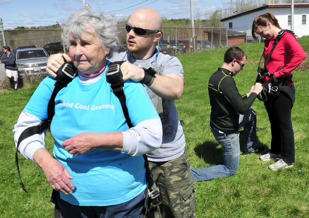 BUCKLE UP: Marjorie Bell, 80, gets buckled into a harness that she and instructor Matt Riendeau used to skydive from a plane over LaFleur Airport in Waterville on Mother’s Day on Sunday, May 11, 2014. One of her daughters, Helen Bell- Necevski of Oakland, gets outfitted with a harness at right.