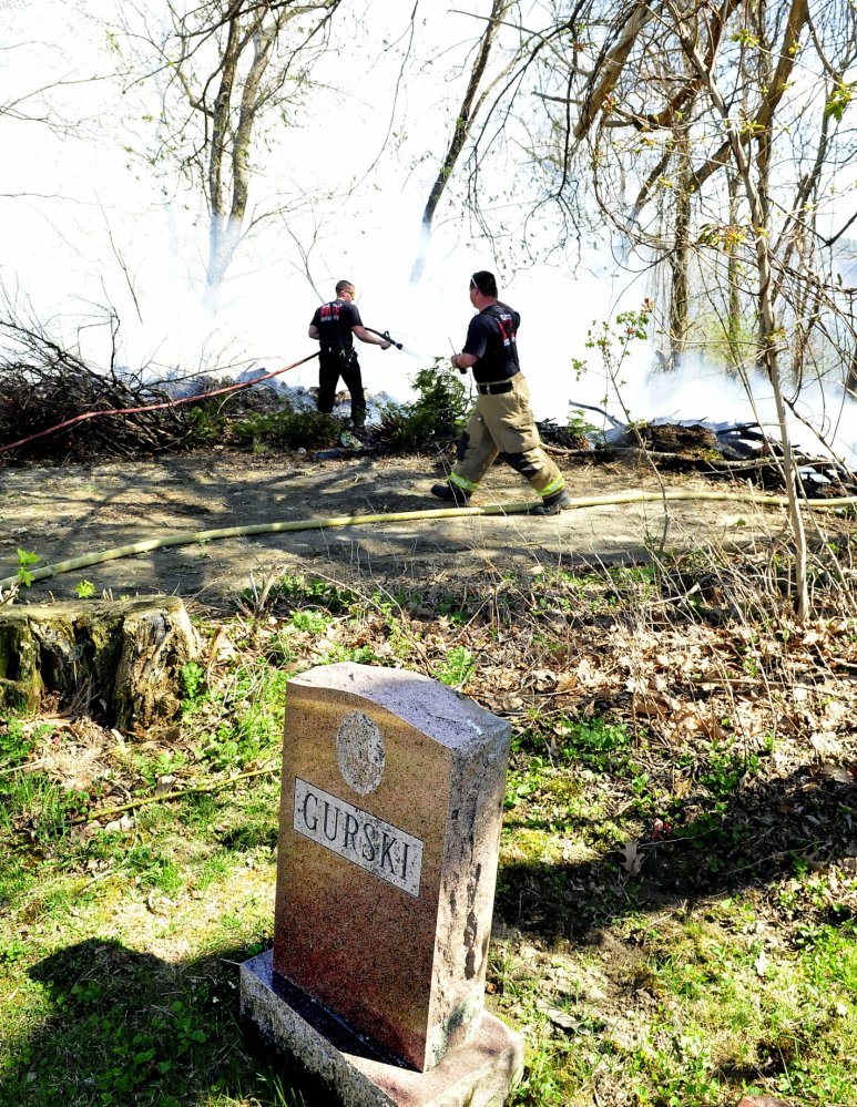 GRAVE CONDITION: Waterville firefighters battle a wind-swept fire in brush and the woods near grave sites that started at the rear of Pine Grove Cemetery on Monday.