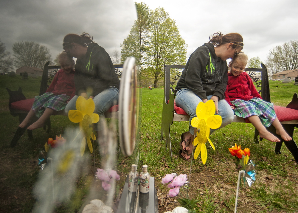 TOGETHER: Riley Souzer, 2, cuddles with her mother Tabitha, at the grave site of her daughter, Avery Jean Lane, at North Fairfield Friends Meeting House cemetery on Thursday. Lane’s grave site was recently vandalized.