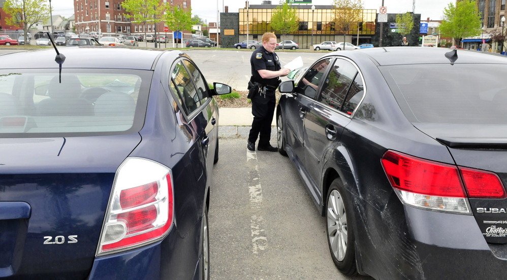 WARNING: Waterville police officer Robert Bouley places a warning and a map for new parking regulations Thursday in The Concourse on a car that was parked longer than the space’s two-hour limit. Behind Bouley is the area where farmers market vendors set up every Thursday.