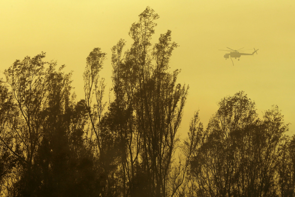 A helicopter transporting water flies over trees during a wildfire Thursday in Escondido, Calif.