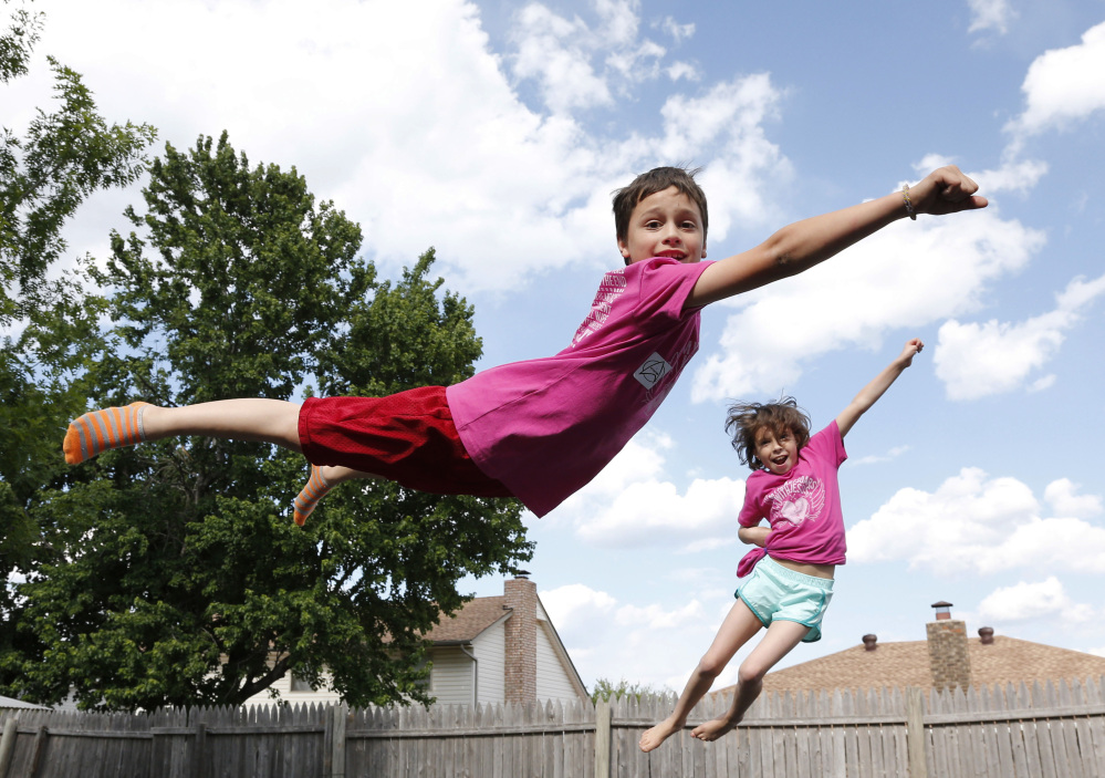 Xavier Delgado, left, and his sister Haley Delgado play on the trampoline in the yard in their new home in Moore, Okla. Xavier was trapped under rubble following the May 20, 2013, tornado at Plaza Towers Elementary school, and Haley was knocked out by debris.