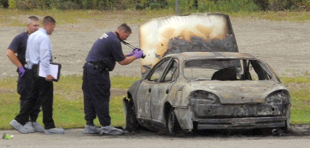 Police investigate a burned vehicle in Bangor on Aug. 13, 2012. The bodies of three Maine residents were found inside the car. Two men are on trial for the killings.