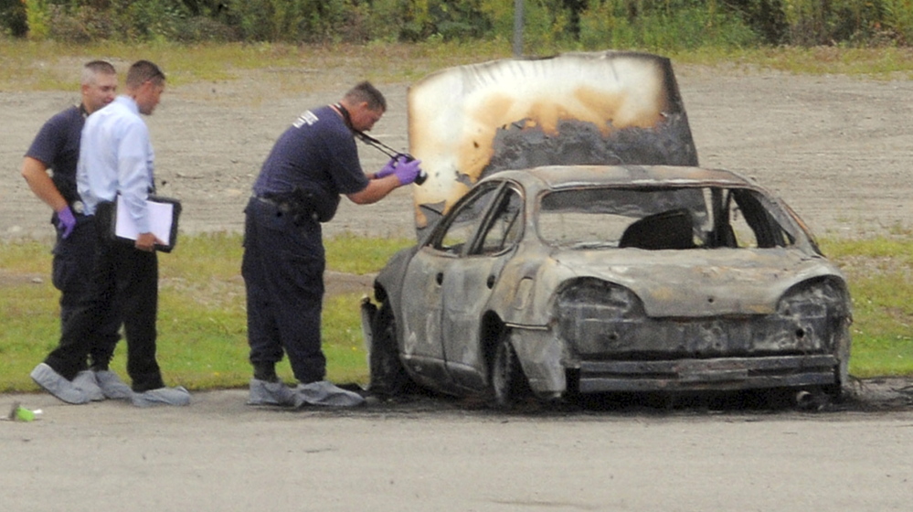 Police investigate a burned vehicle in Bangor in August 2012. Three bodies were found inside the parked car.