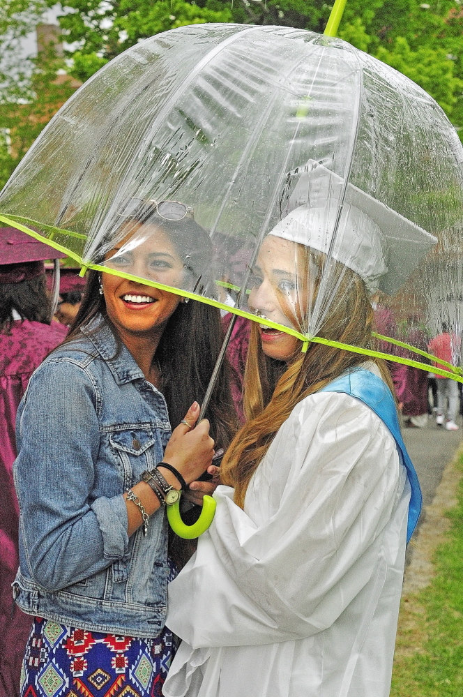 SHIELDED: Carmen Adams, left, holds an umbrella over herself and graduate Sarah Grenier as a shower blows through before the graduation ceremony Saturday at Kents Hill School in Readfield.