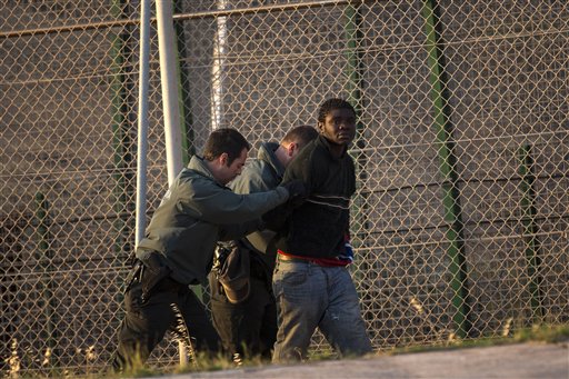 A sub-Saharan migrant is detained by Spanish guards after scaling a fence that divides Morocco and the Spanish enclave of Melilla early Wednesday morning.