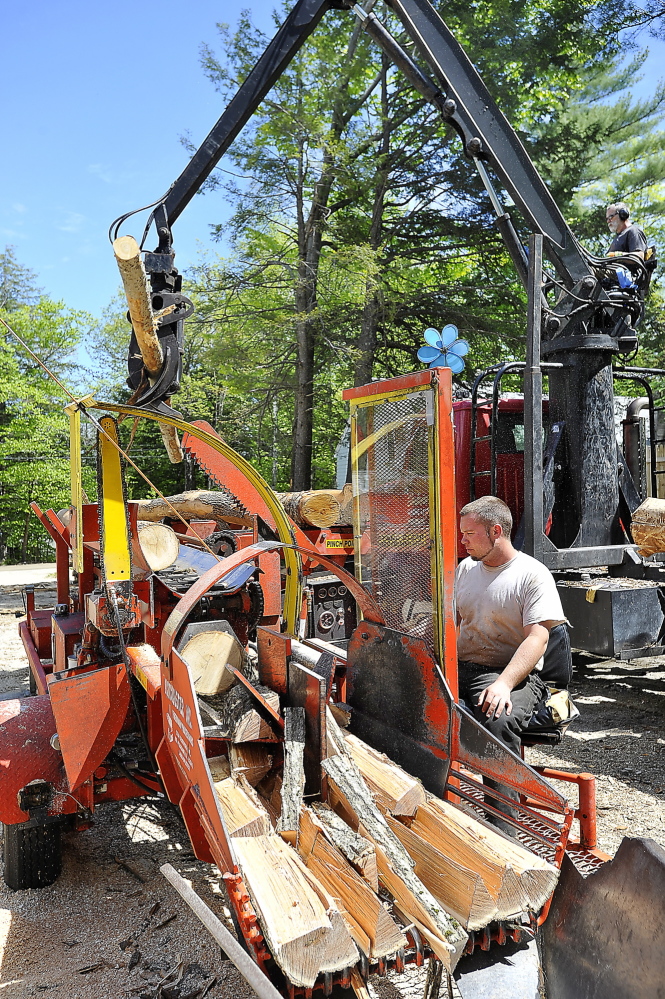 Mark Killinger, back, owner of Atlantic Firewood, adds hardwood logs to the line as his son, Mike Killinger, owner of Maine Logging, tends the cutting and processing machine as they work together to cut and process firewood.
